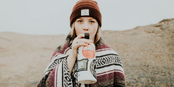 person wearing beanie and shawl drinking from water bottle