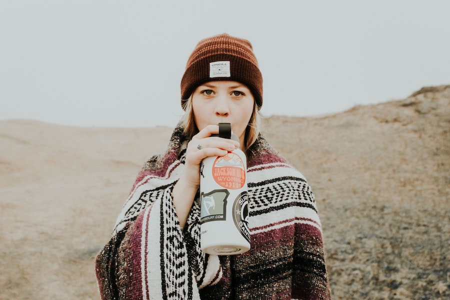person wearing beanie and shawl drinking from water bottle