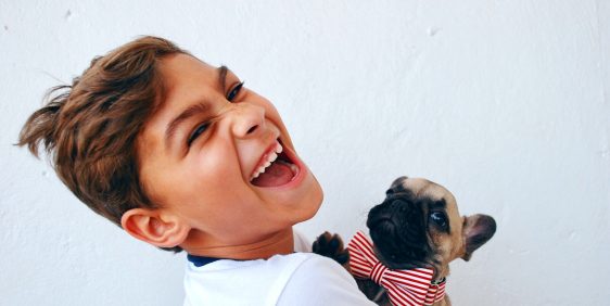 young boy in white shirt laughing with puppy wearing red bow tie