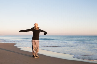 Cancer and oral care for lady in black shirt with arms spread at beach